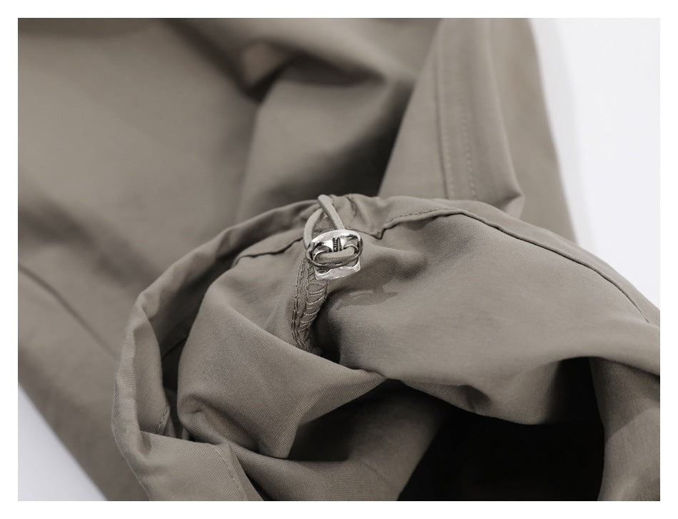 Close-up of taupe garment fabric with a small metal buckle and stitched trim.