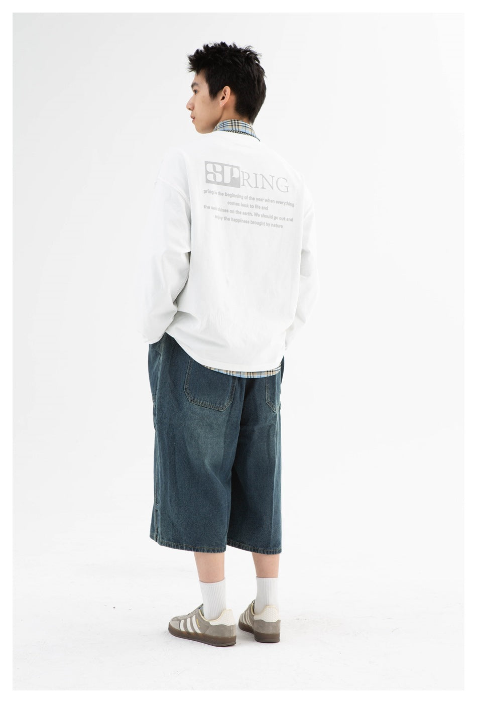 Back view of model in the white long-sleeve top with large SPRING graphic and small text, with denim shorts