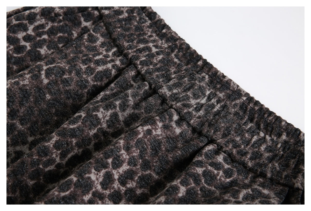 Close-up of the gathered elastic waistband and pleats on dark brown and black leopard-print trousers.