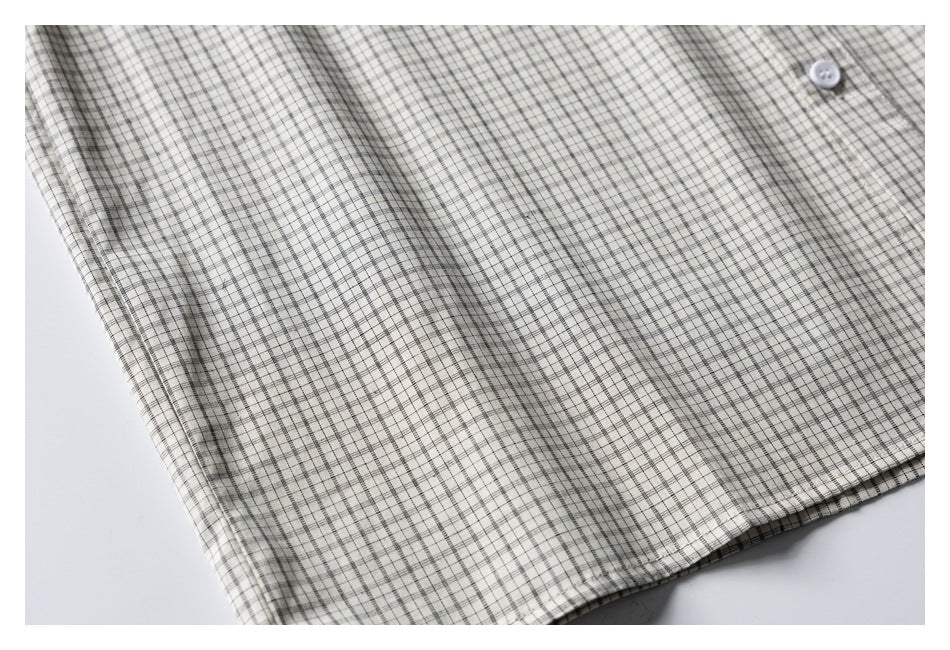 Partial flat-lay front view of a cream shirt with fine black-and-gray plaid and a white button.