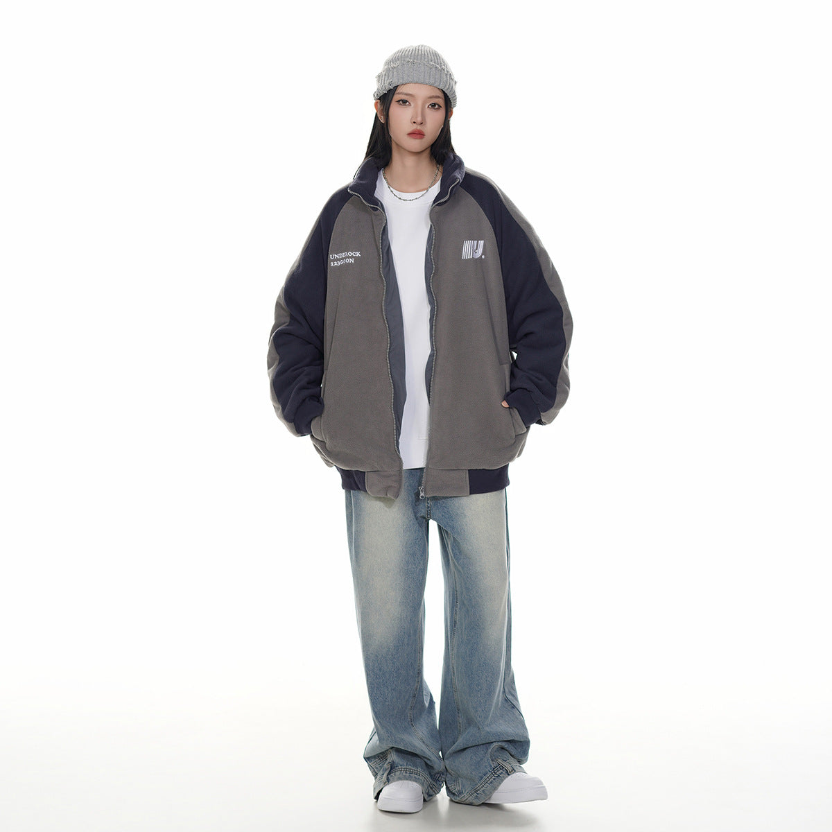 Full-length model wearing an open charcoal gray and navy zip-up jacket over a white shirt with loose light-wash jeans.