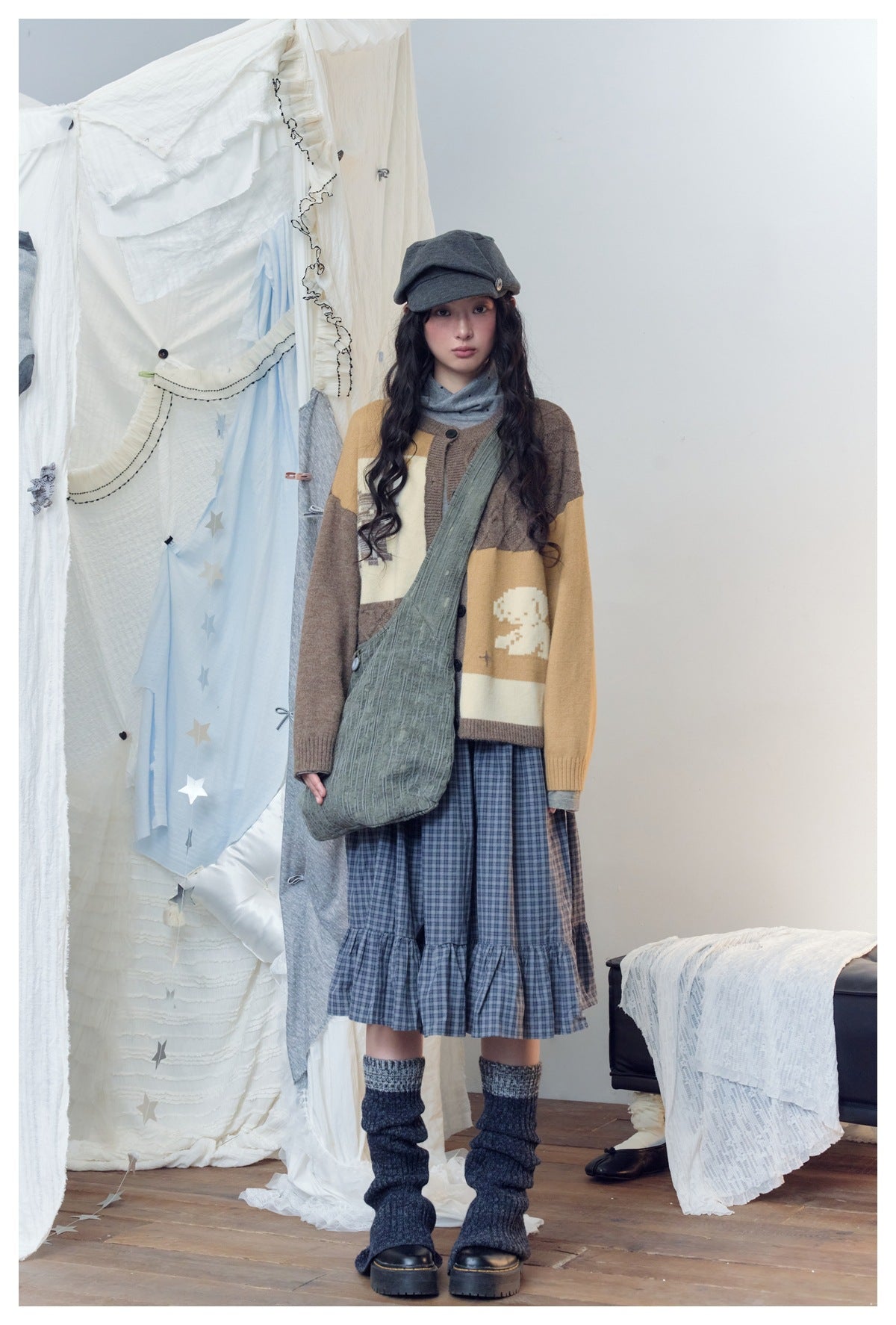 Model wearing the brown, tan and cream cardigan with a plaid ruffle skirt, cap, gray crossbody bag and leg warmers