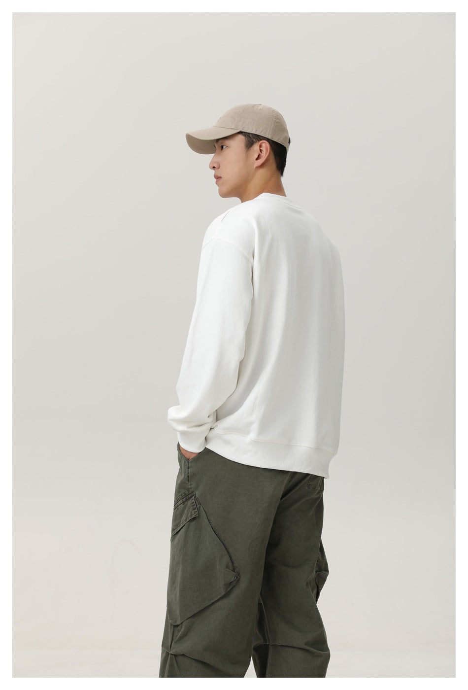 Model in a white sweatshirt seen from behind with olive cargo pants and a beige cap