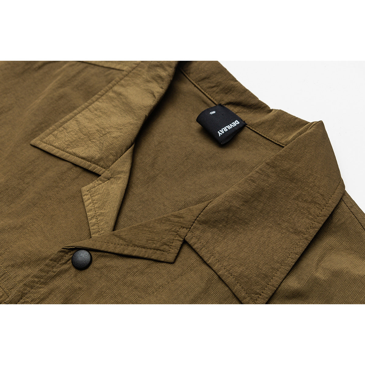 Close-up of an olive-brown jacket collar, lapel, black snap button, and attached black brand tag.