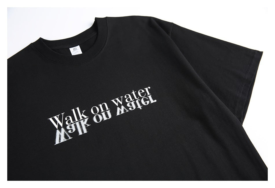 Angled close view of a black T-shirt with a white “Walk on water” chest print and reflection effect.