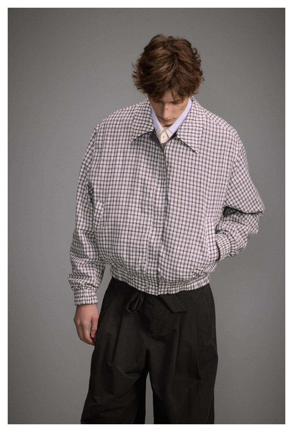 Model looking down while wearing a light plaid zip-front jacket with a wide collar and elastic hem.