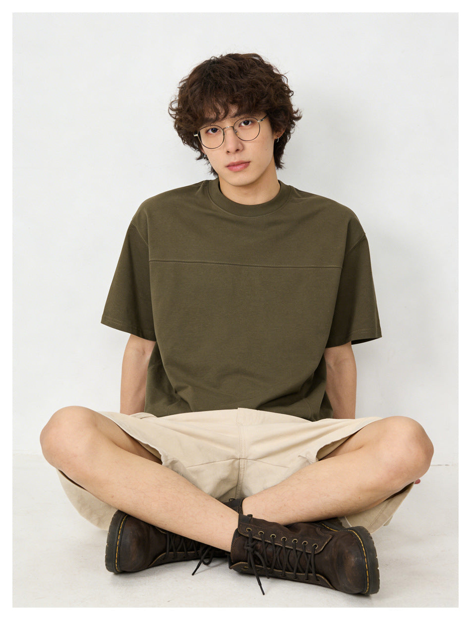 Seated model wearing an olive short-sleeve crew-neck T-shirt with a horizontal chest seam.