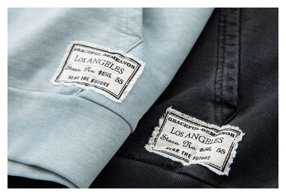 Close-up of light blue and black hoodie fabric with sewn rectangular English-text patches.
