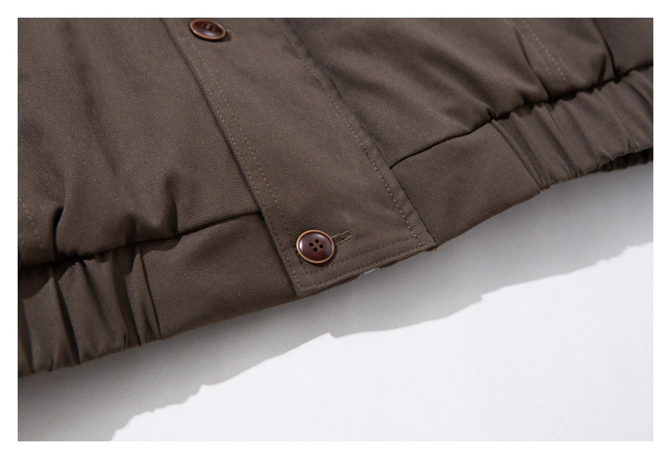 Close-up of a dark brown coat hem with elastic gathering and a buttoned tab.