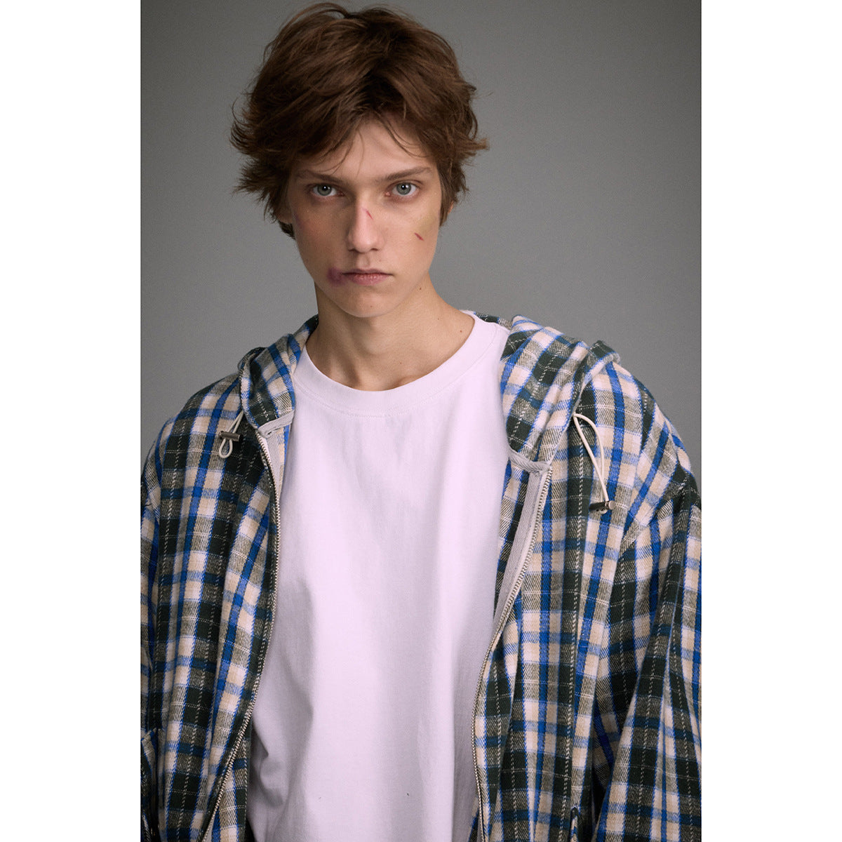 Model wearing an open blue, black, and cream plaid hooded zip jacket over a white T-shirt.