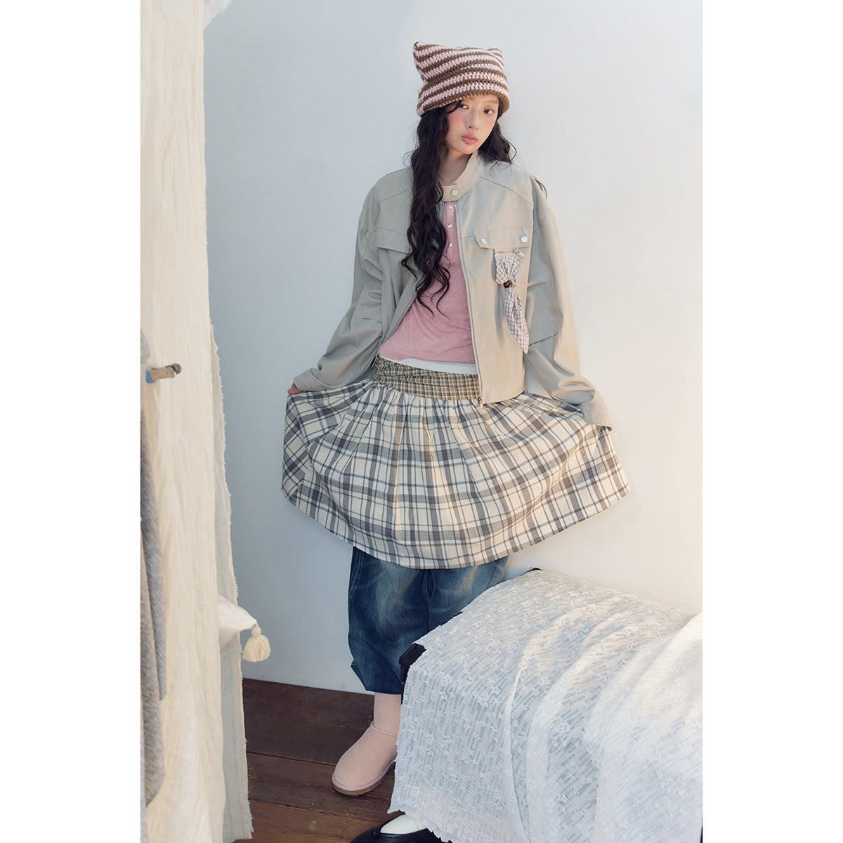 Model holds out a gray-and-cream plaid skirt over jeans, with a light gray jacket and pink top.