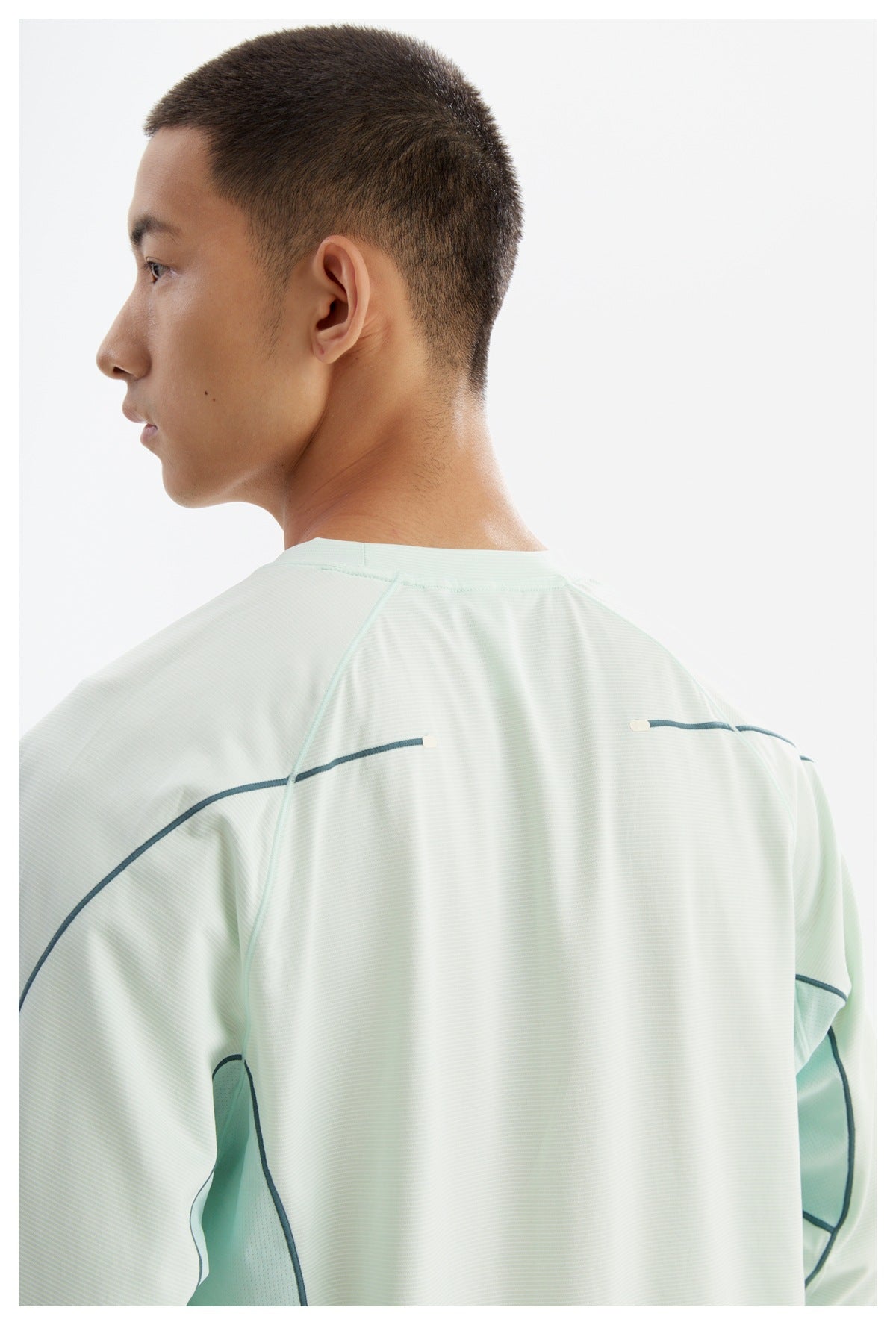 Close rear view of a pale mint shirt worn by a man, with dark curved piping across the back and sleeves.
