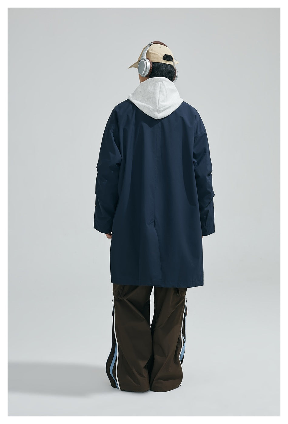 Rear view of a person wearing a long navy coat with a light gray hood and dark trousers.