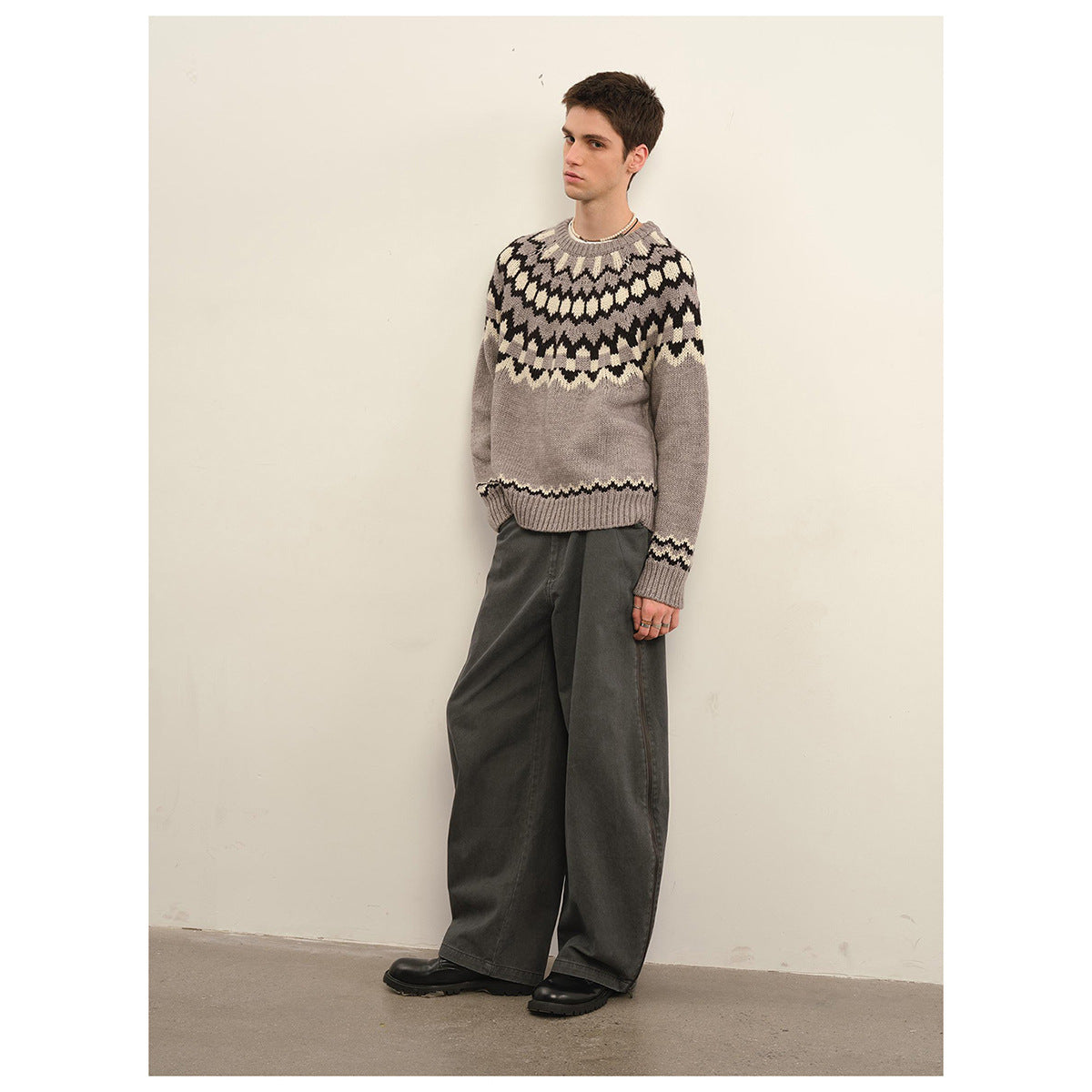 Full-length view of a model in a taupe gray geometric-yoke sweater, wide dark trousers, and black shoes.