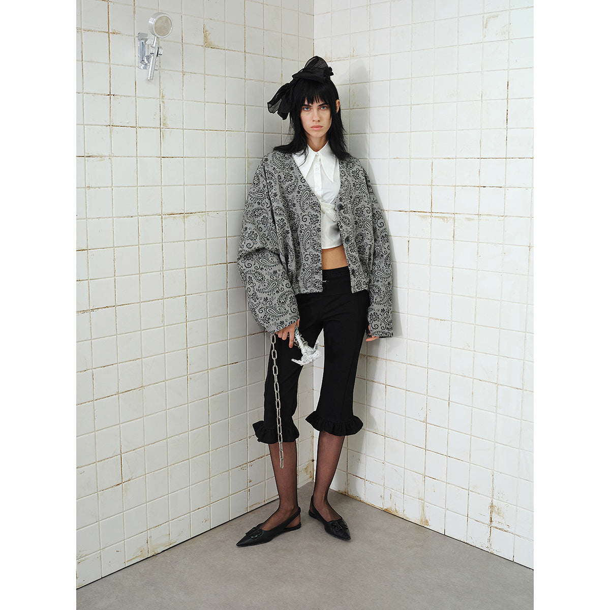 Model wearing an oversized gray paisley button-front jacket with black cropped ruffle-hem pants, shown at a slight angle.