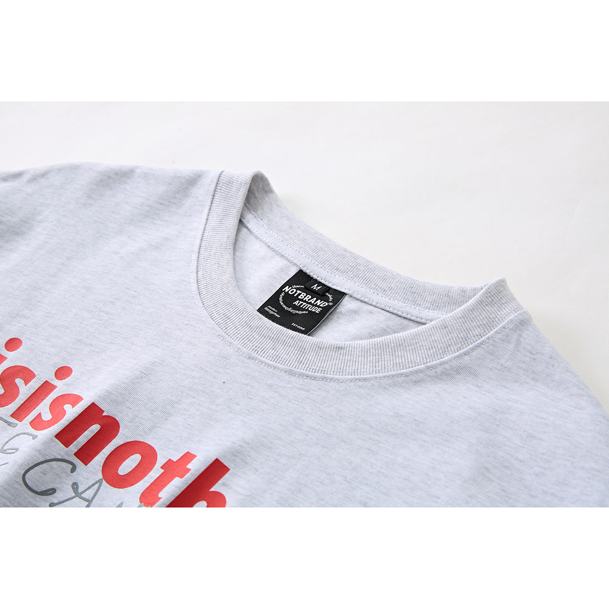 Close-up of a light gray T-shirt collar, neck label, and partial red chest print.