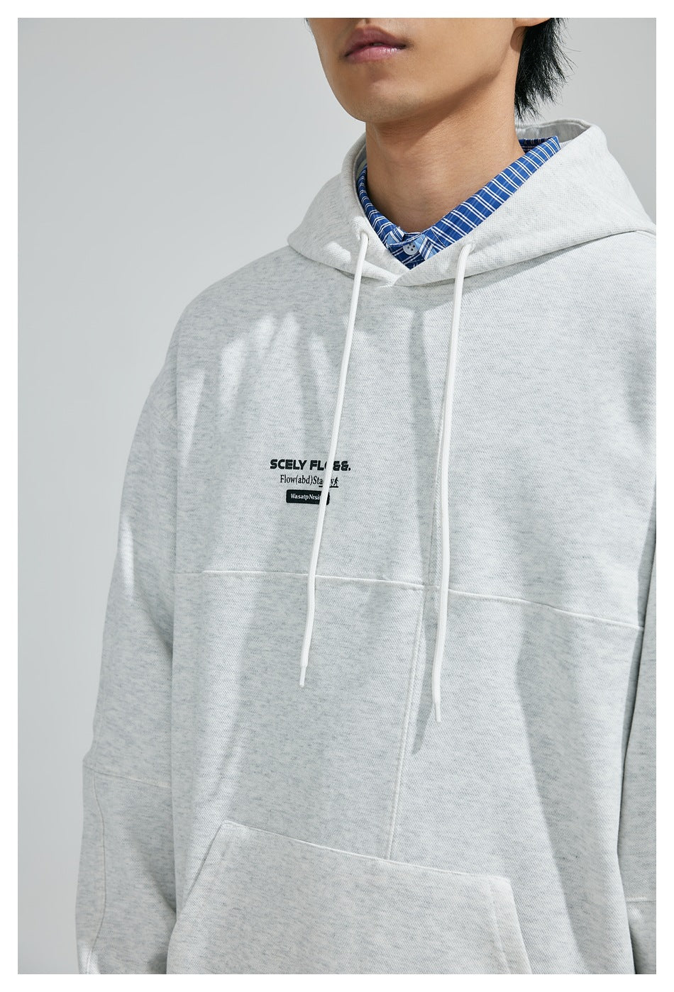 Close-up of a model wearing a light gray hooded sweatshirt with white drawstrings and small black chest text.