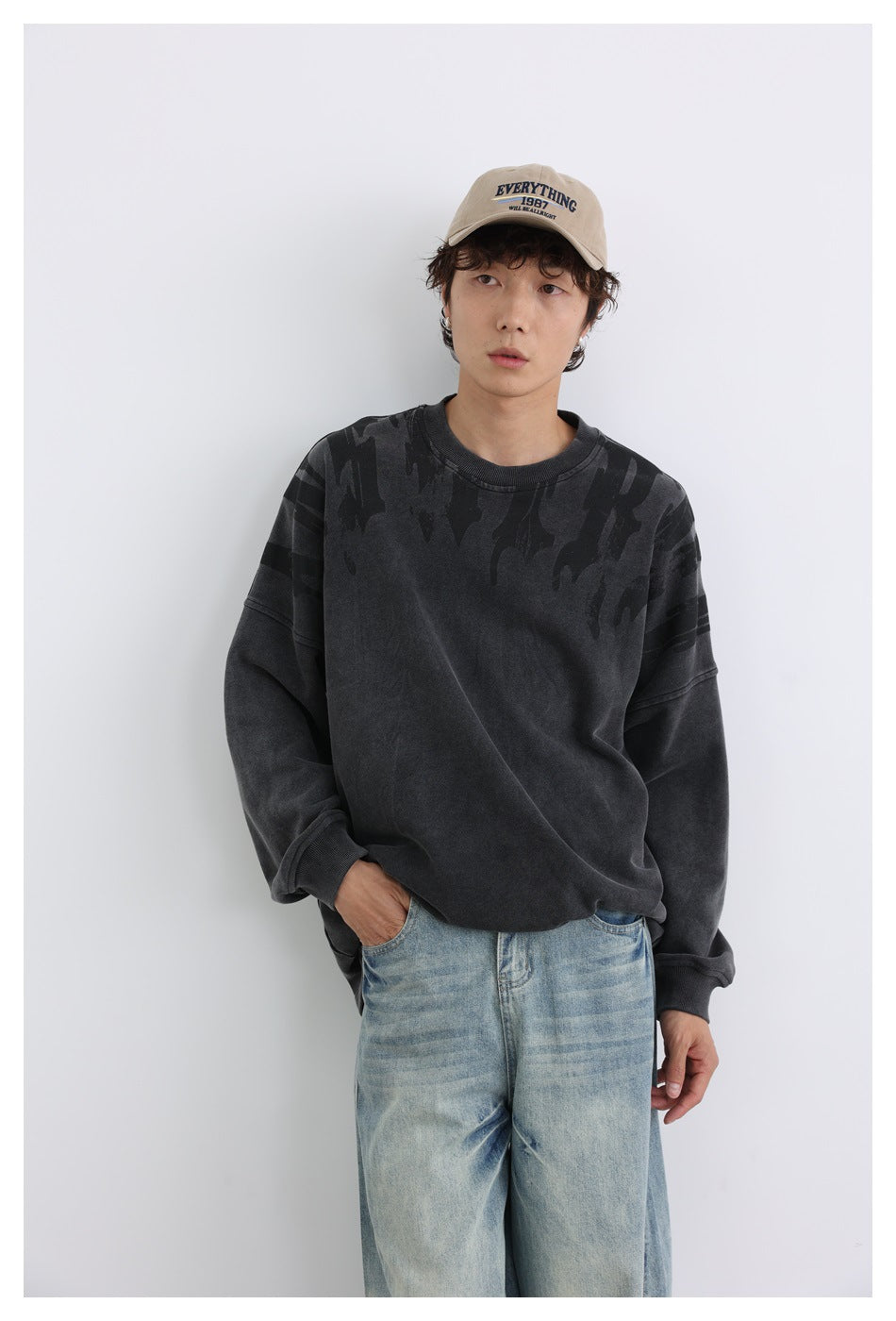 Model wearing a charcoal oversized crewneck sweatshirt with dark shoulder graphics and faded blue jeans.