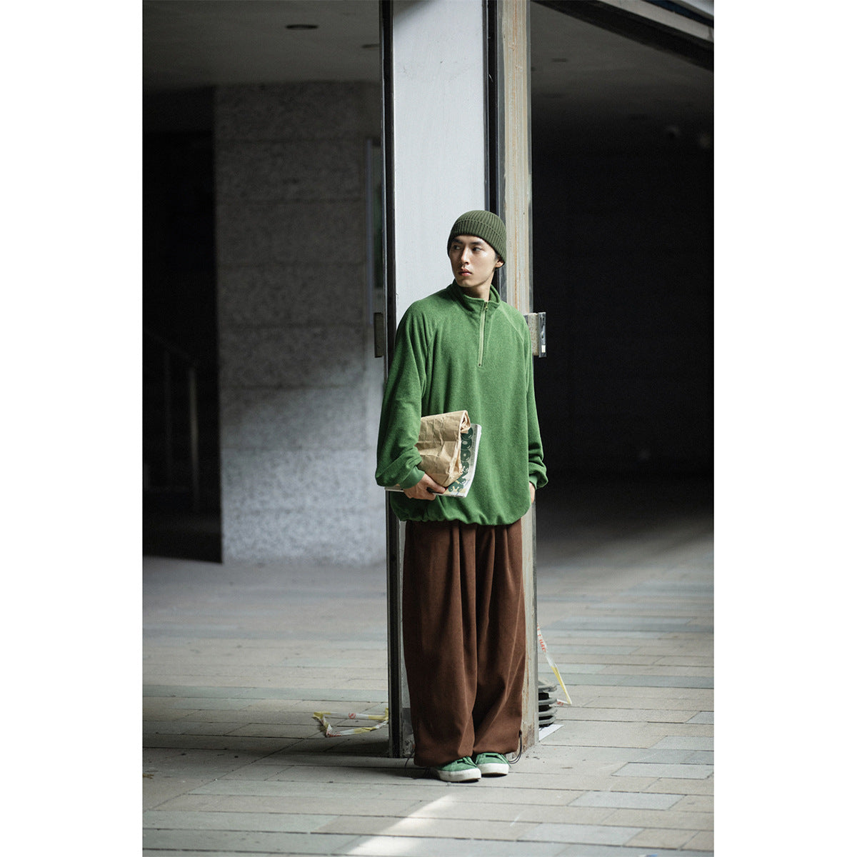 Person wearing a green quarter-zip pullover, brown wide-leg pants and an olive knit beanie.
