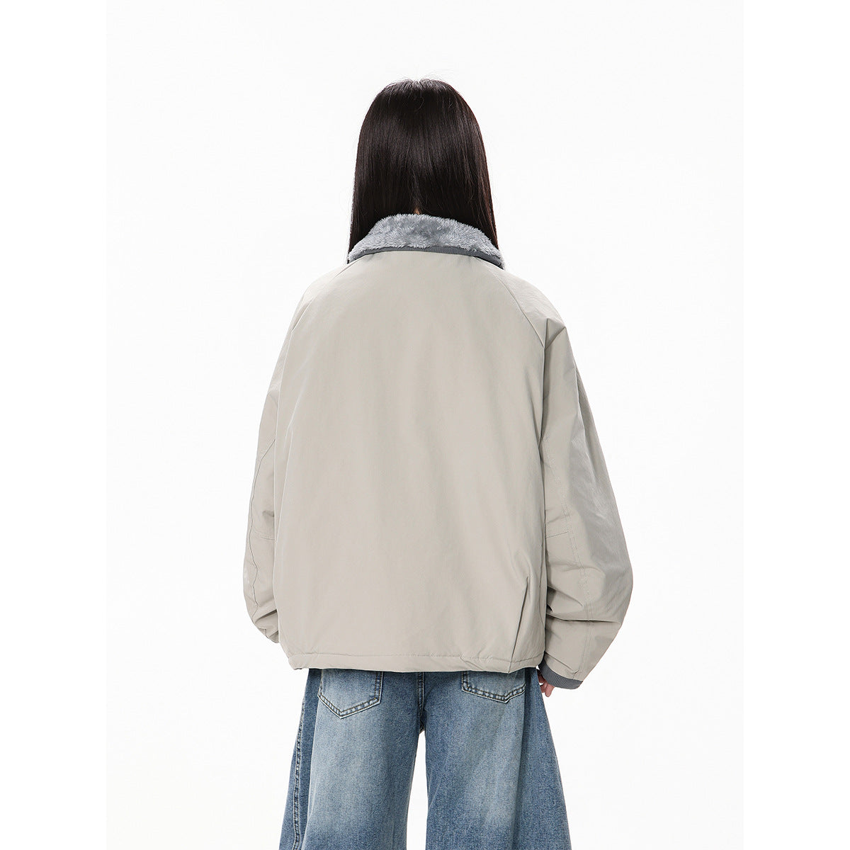Back view of a model wearing a light gray oversized jacket with a gray plush collar and wide blue jeans.