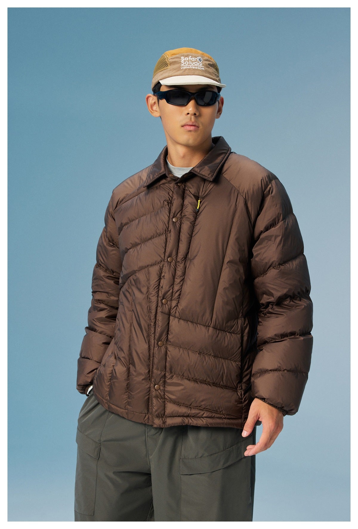 Model in a front view wearing a dark brown quilted jacket with a collar, snap front, and yellow zipper pull.