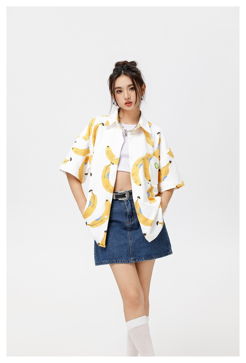 Model wearing an oversized white short-sleeve button-up shirt with a yellow banana print and a blue denim skirt.