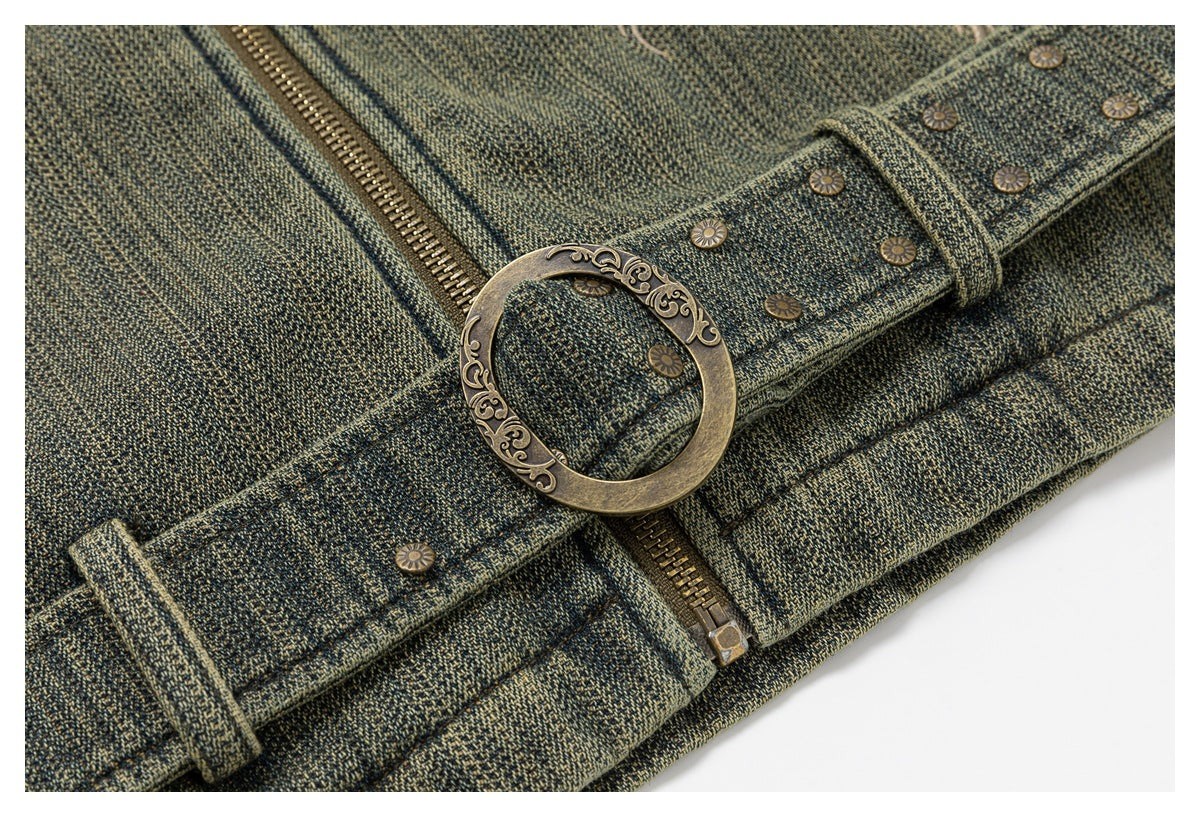 Close-up of an ornate antique-brass ring buckle, studded belt, and zipper on olive-gray fabric.