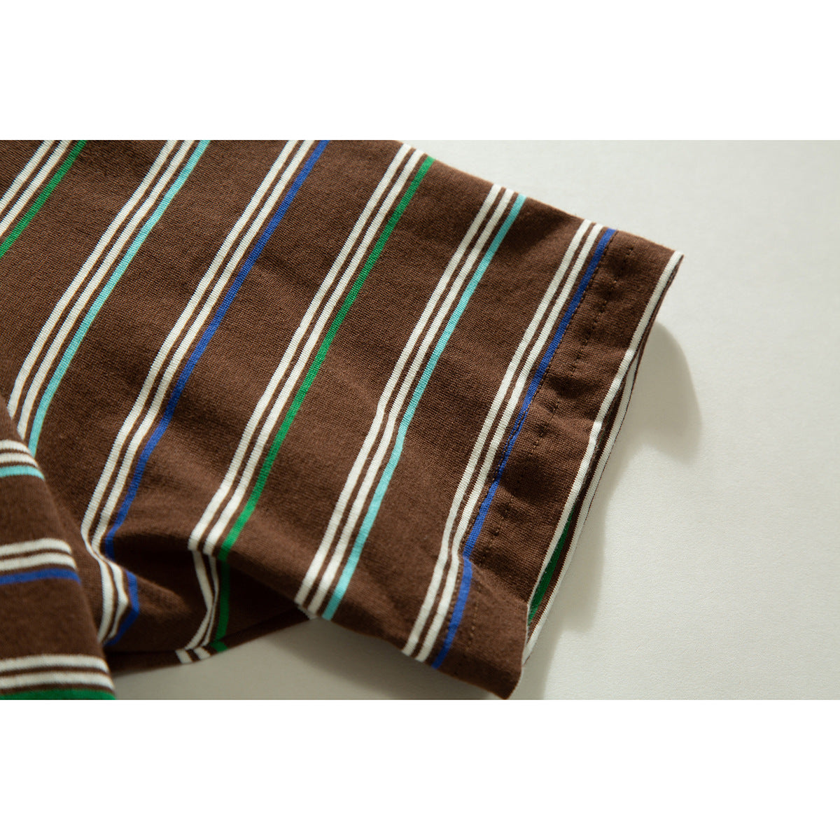 Close-up of the brown polo shirt's short sleeve and hem, patterned with cream, green, turquoise, and blue stripes.