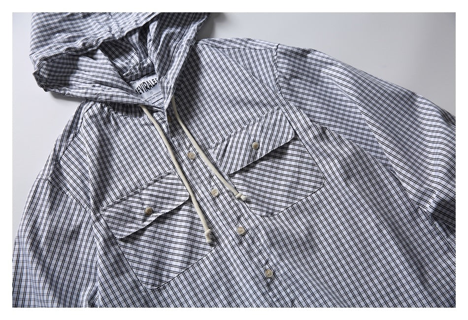 Close-up of a white-and-black checked hooded shirt showing its button placket and two flap chest pockets.