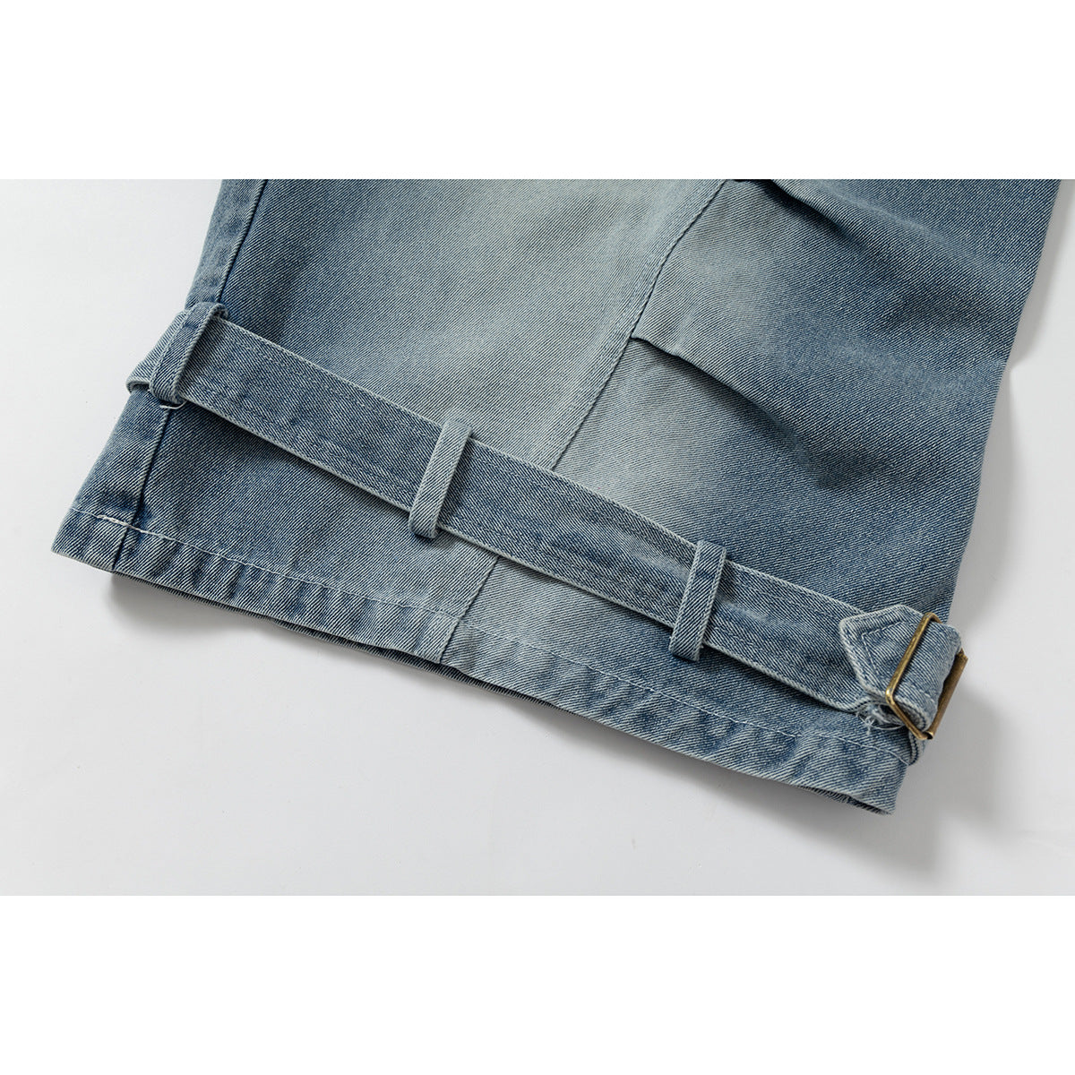 Close-up of a blue denim trouser hem with a wide adjustable strap, belt loops and a metal buckle.
