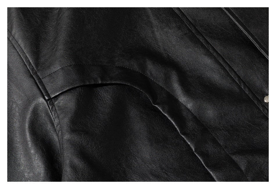 Close-up of curved stitched seams on a black leather-look garment, with a metal snap at the edge.