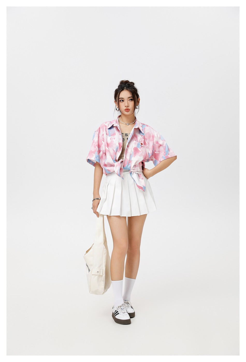 Model wearing a pink and blue abstract-print short-sleeve button-up shirt tied at the waist with a white pleated skirt.