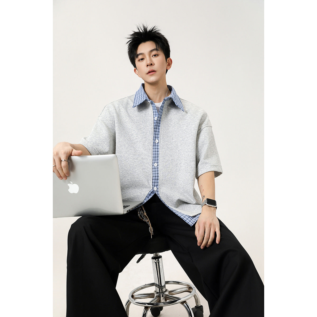 Seated model wearing a light gray short-sleeve button-up shirt with blue plaid trim.