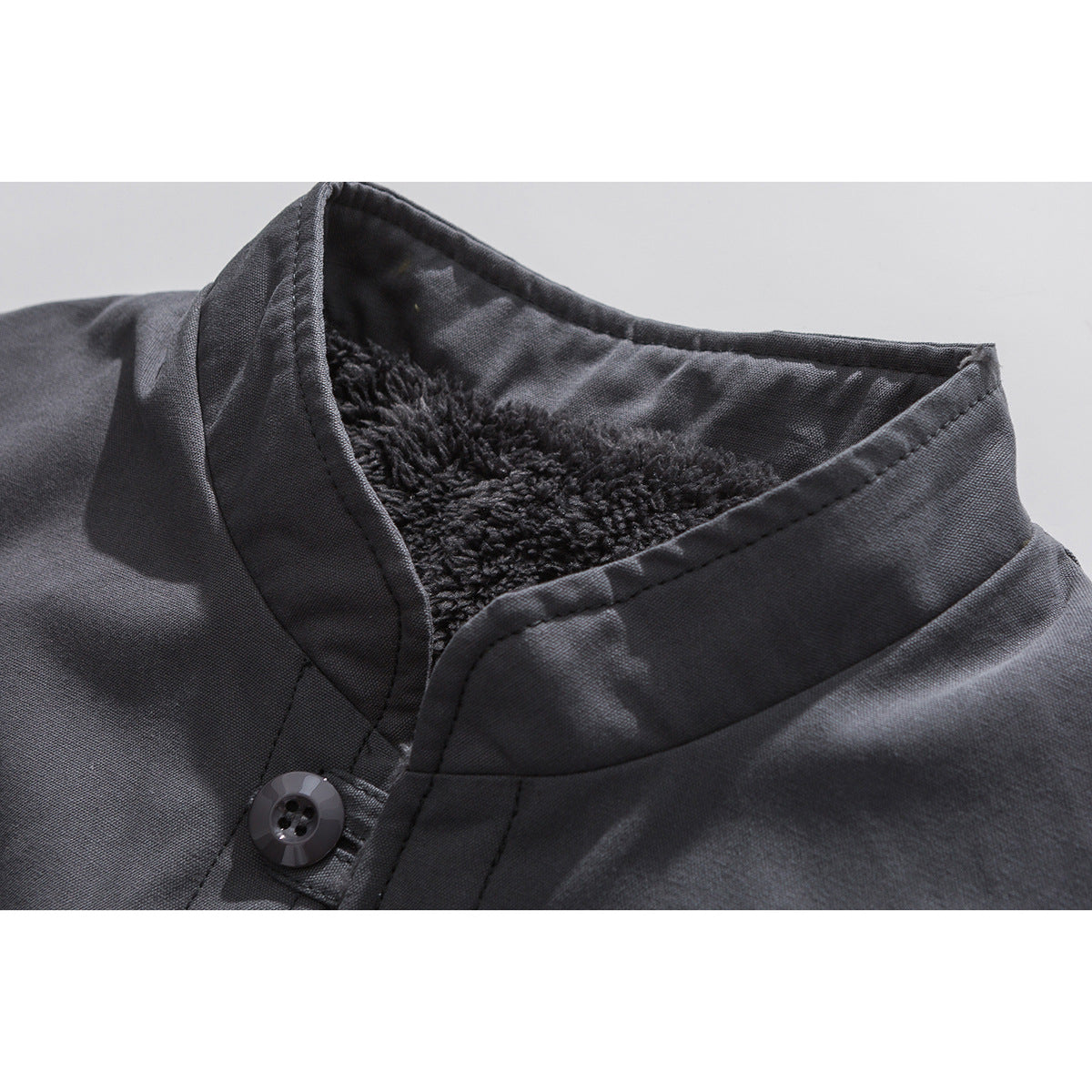 Close-up of a charcoal coat’s stand collar, showing plush dark lining and a button closure.