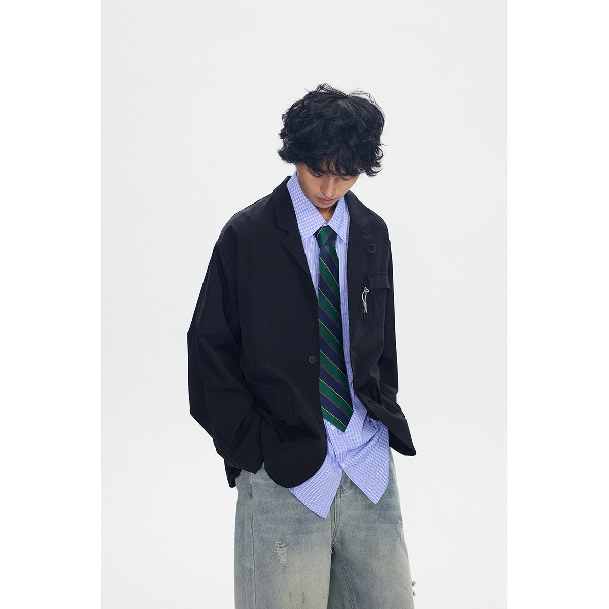 Model wearing a loose black blazer over a blue striped shirt and green striped tie, with faded jeans.