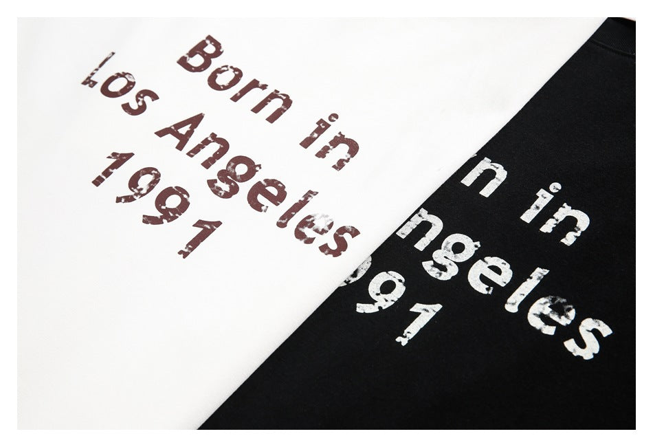 Close-up of white and black T-shirts printed with distressed text reading “Born in Los Angeles 1991.”