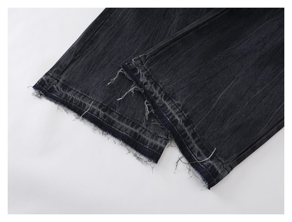 Close-up of dark jeans showing raw, frayed hems and a slit at the leg opening.