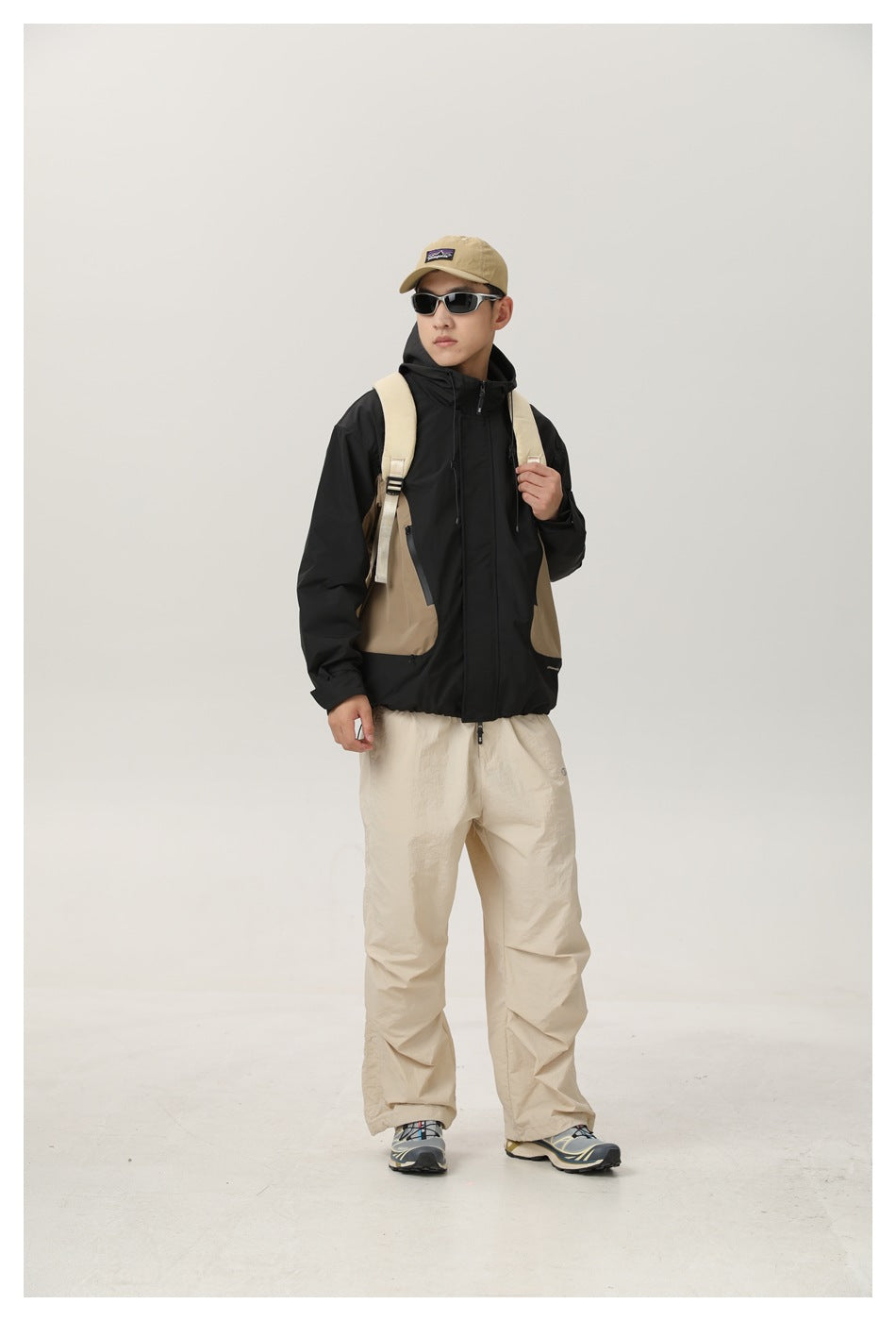 Front view of a model wearing a black hooded jacket with tan side panels and beige trousers.