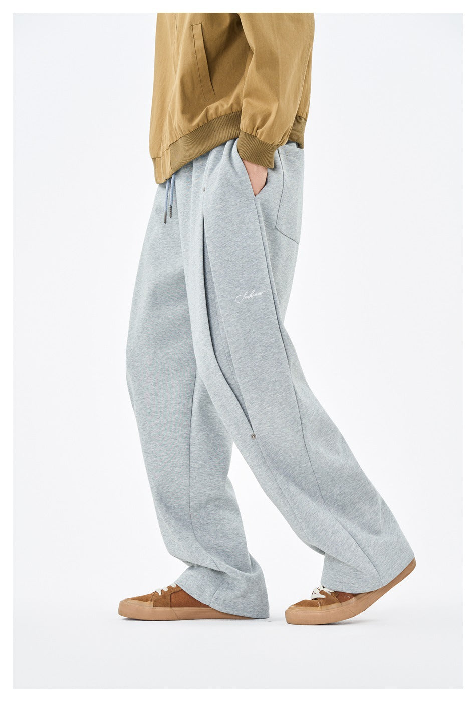 Side view of a model wearing light gray wide-leg drawstring pants with a side pocket and small embroidered script.