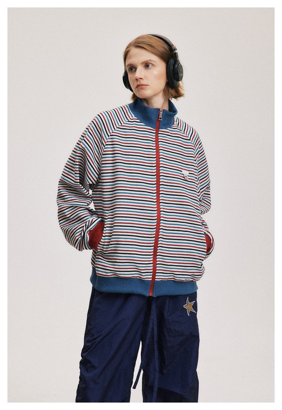Model wearing a striped zip jacket with a blue collar and hem, red cuffs, and a small tomato patch on the chest.