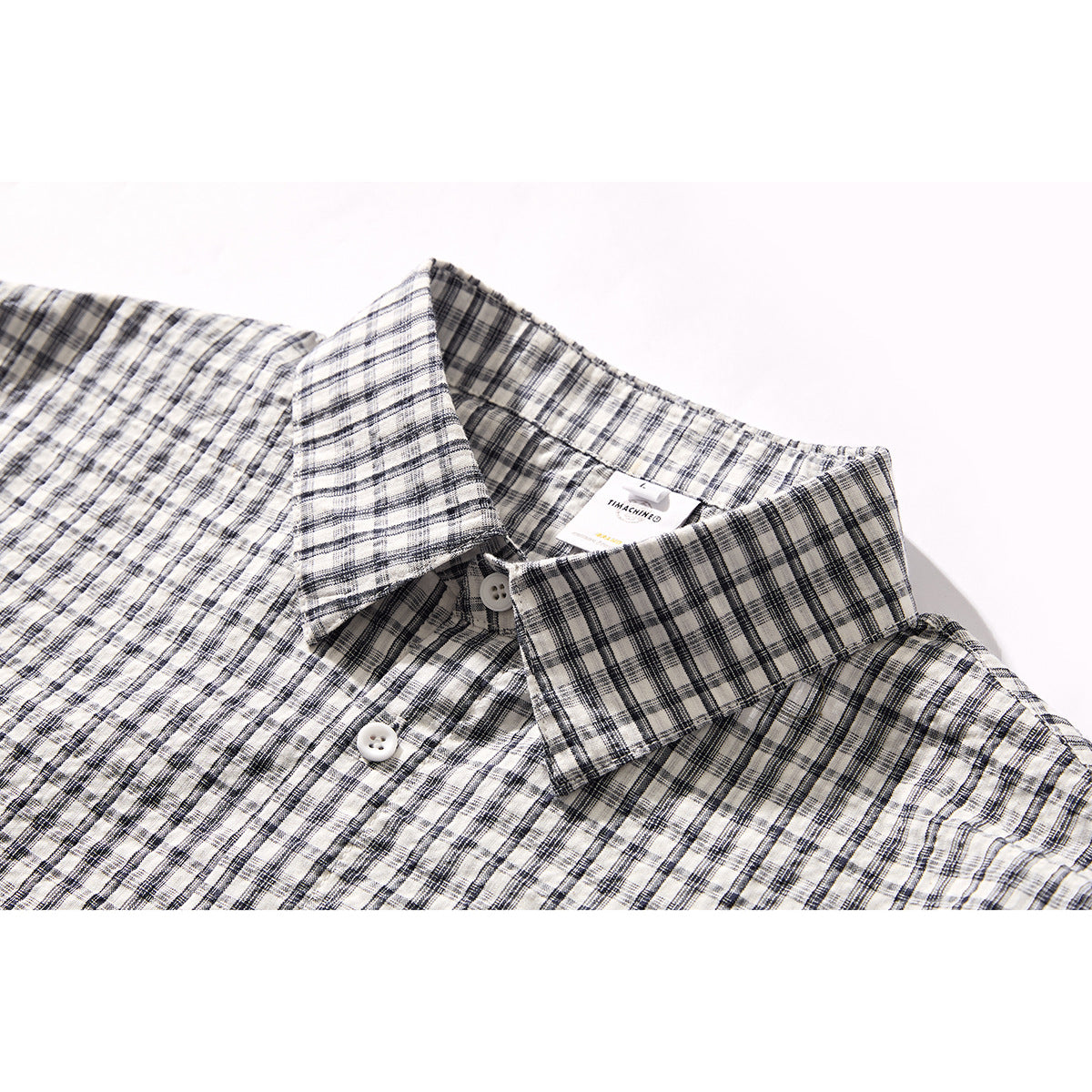 Close-up of a black-and-white plaid shirt collar, neckline label, and white buttons.