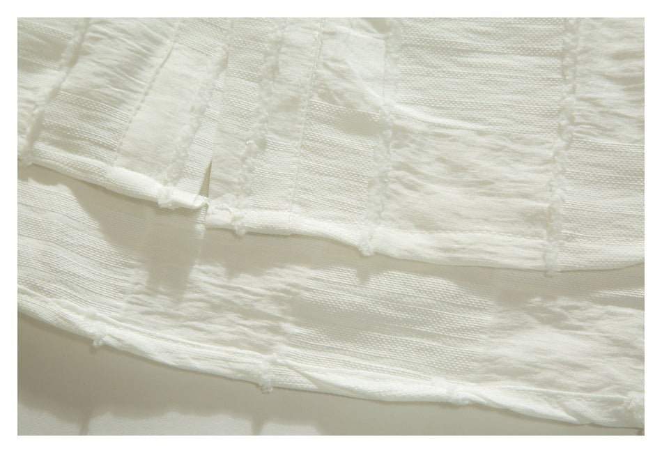 Close-up of overlapping ivory fabric layers with textured panels and raw, softly frayed edges.
