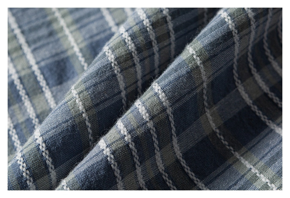 Macro view of blue-gray plaid fabric folded to show its woven texture and raised white stripes.