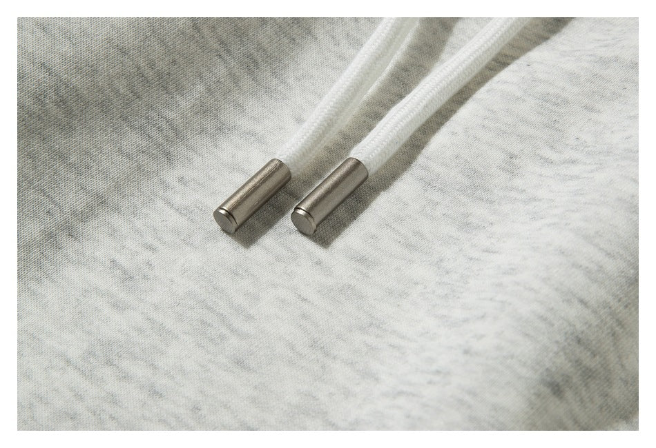 Close-up of white drawstrings with metal tips against light heather-gray sweatpants.