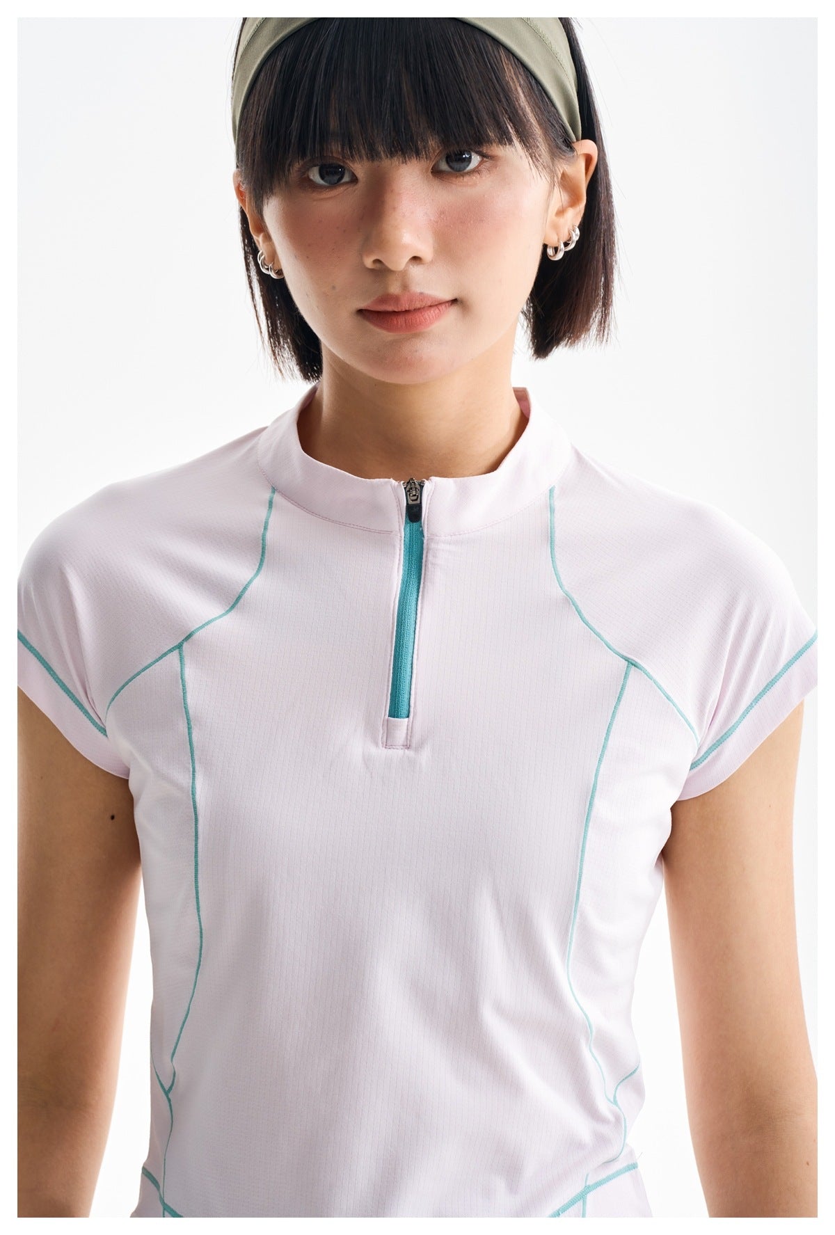 Model wearing a pale pink short-sleeve zip-neck top with turquoise contrast seams, shown from the front.