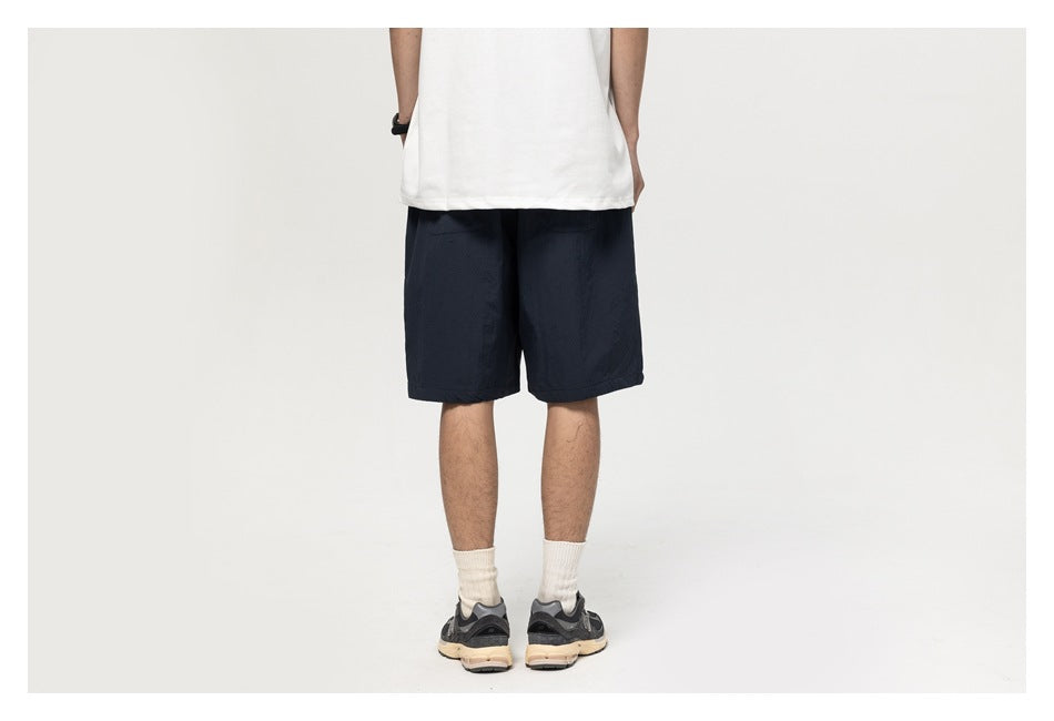 Back view of a man wearing navy knee-length shorts with a white tee and cream socks