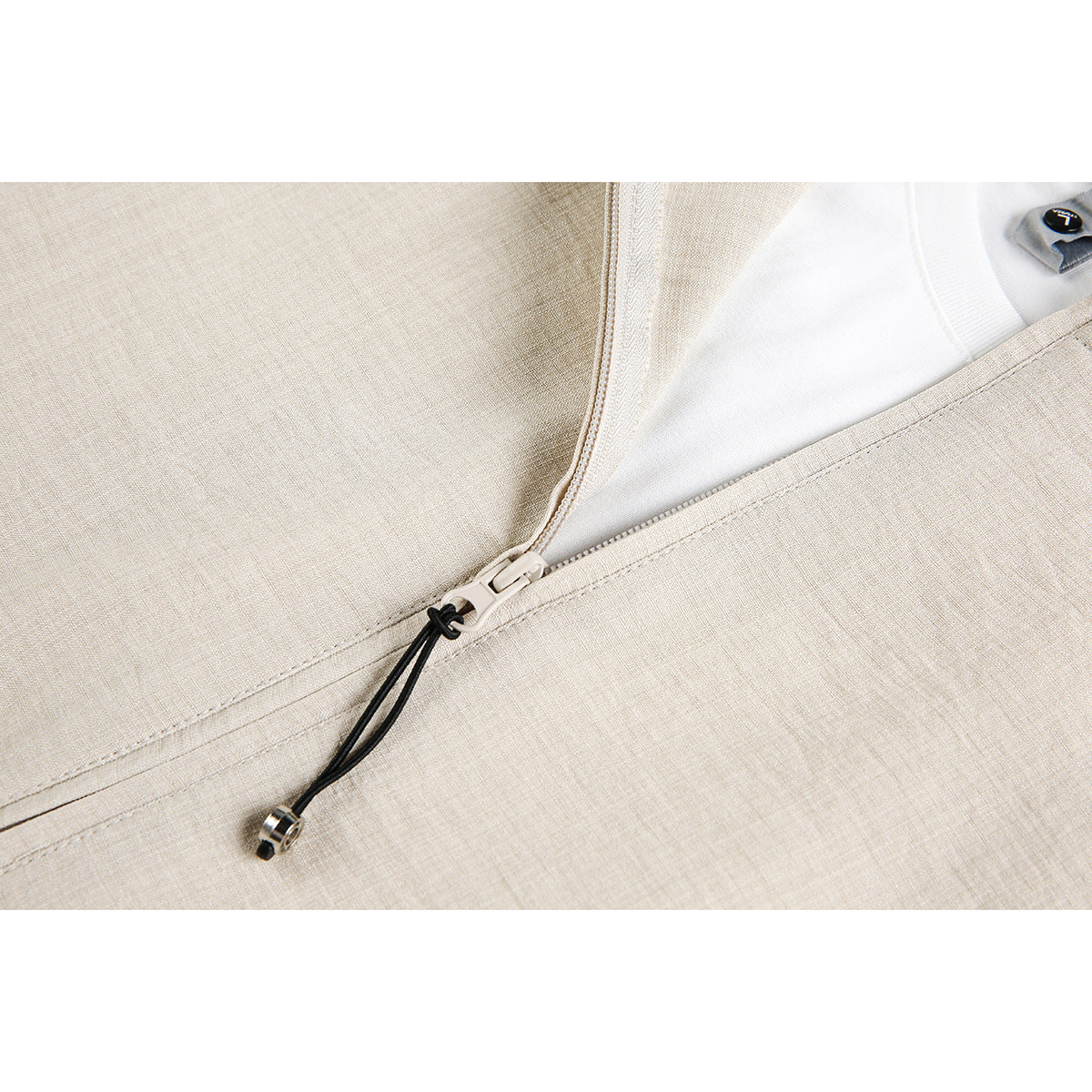 Close-up of a cream jacket's front zipper, black cord pull, stitching, and white inner layer.