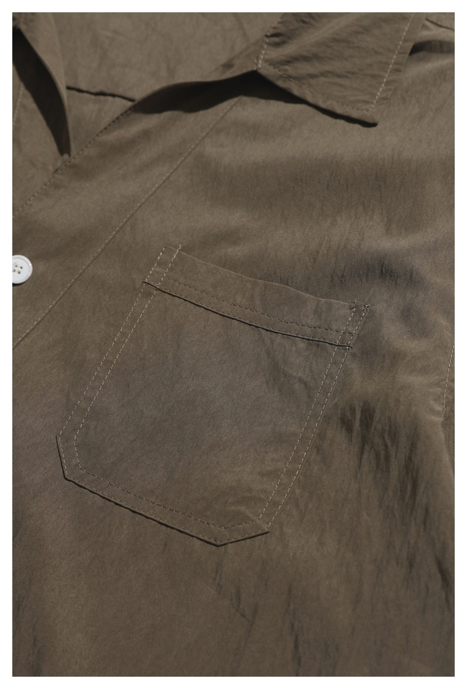 Close-up of a brown shirt's large stitched chest pocket and pointed collar edge.