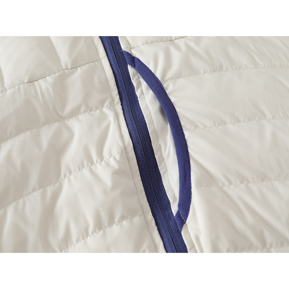Close-up of an ivory quilted jacket with a dark blue zipper and attached fabric pull loop.
