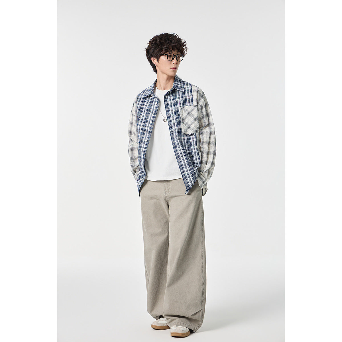 Model in an open blue-and-gray plaid shirt, white tee and loose gray trousers, shown at a slight angle.